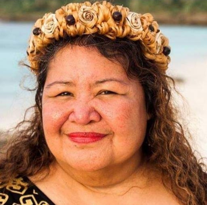 Headshot of Cinta M. Kaipat, an indigenous woman with long brown hair, wearing a headpiece and smiling at the camera. She is standing against a beach background. Picture by Earthjustice.